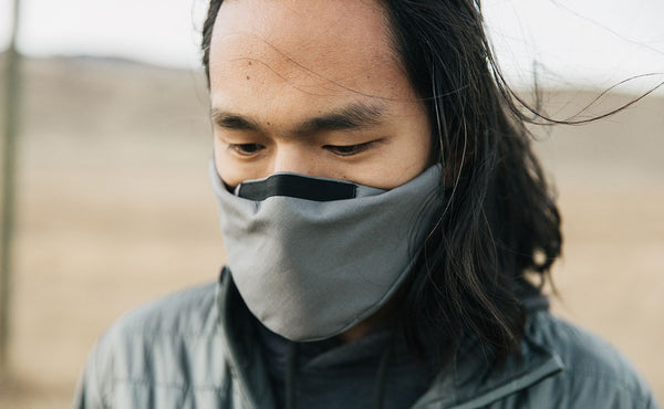 Person standing outdoors in a grassy field wearing the V6 Mask in True Grey.